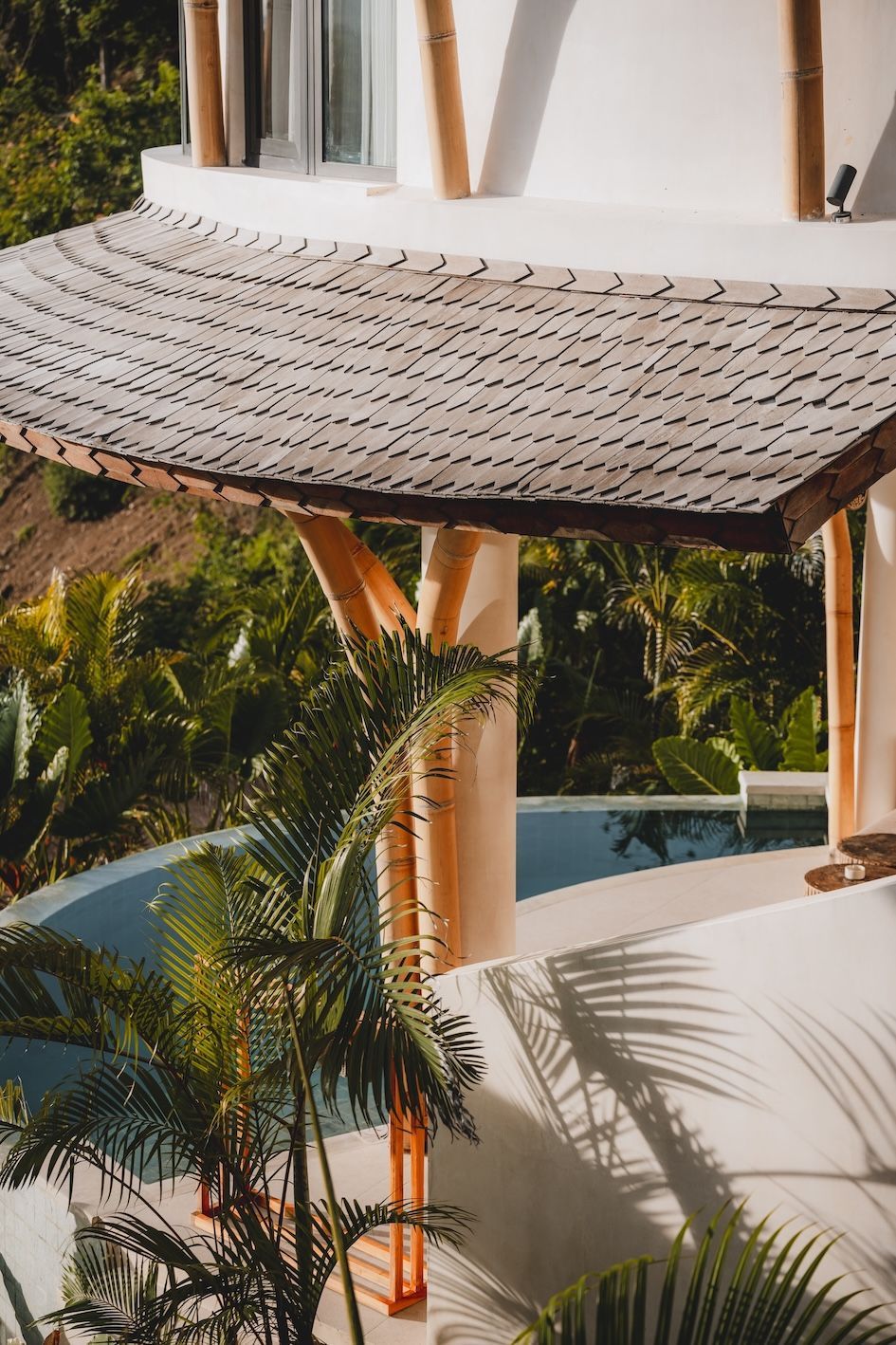 Curved thatched roof over a tropical resort pool with palm trees and white buildings