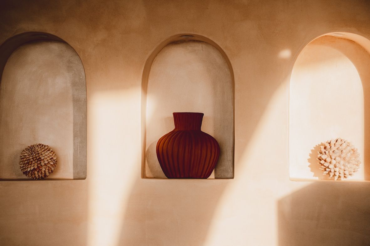Three arched wall niches with decorative vases and dried flowers in warm sunlight