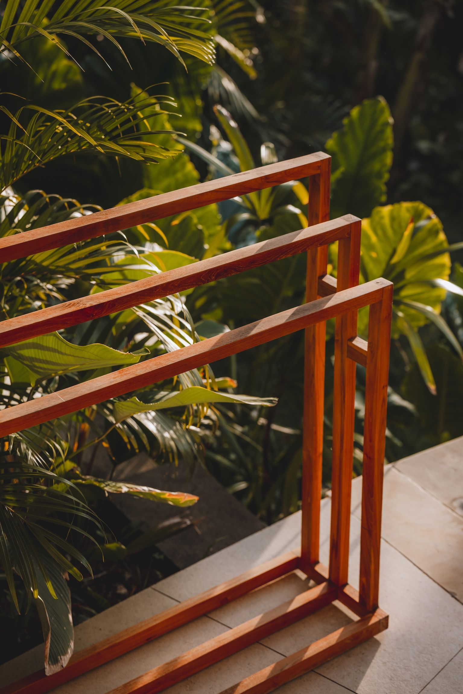 Orange metal railing beside lush green tropical plants and a tiled walkway