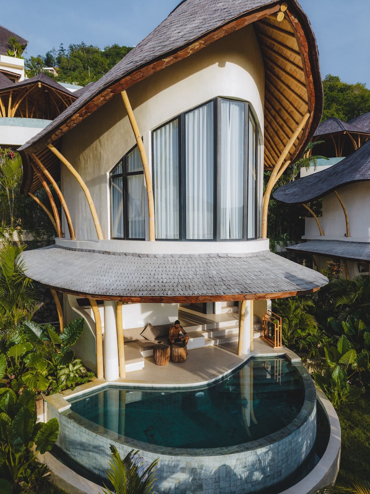 Modern villa with curved roof and pool overlooking lush tropical greenery