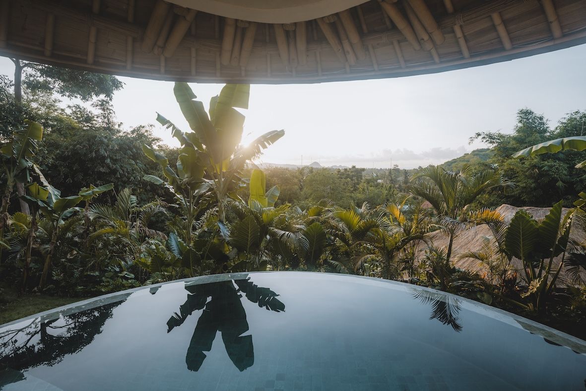 Sunlit tropical resort view reflected in a glossy table under a thatched roof