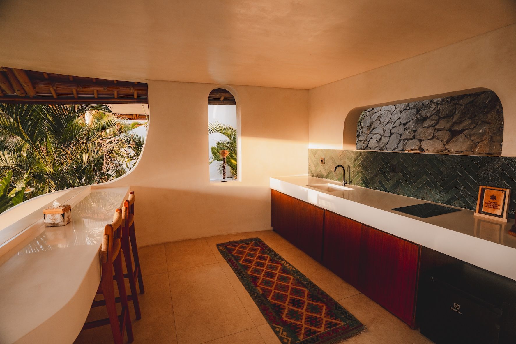 Modern kitchen with stone backsplash, long counter, and warm-toned interior with open window view