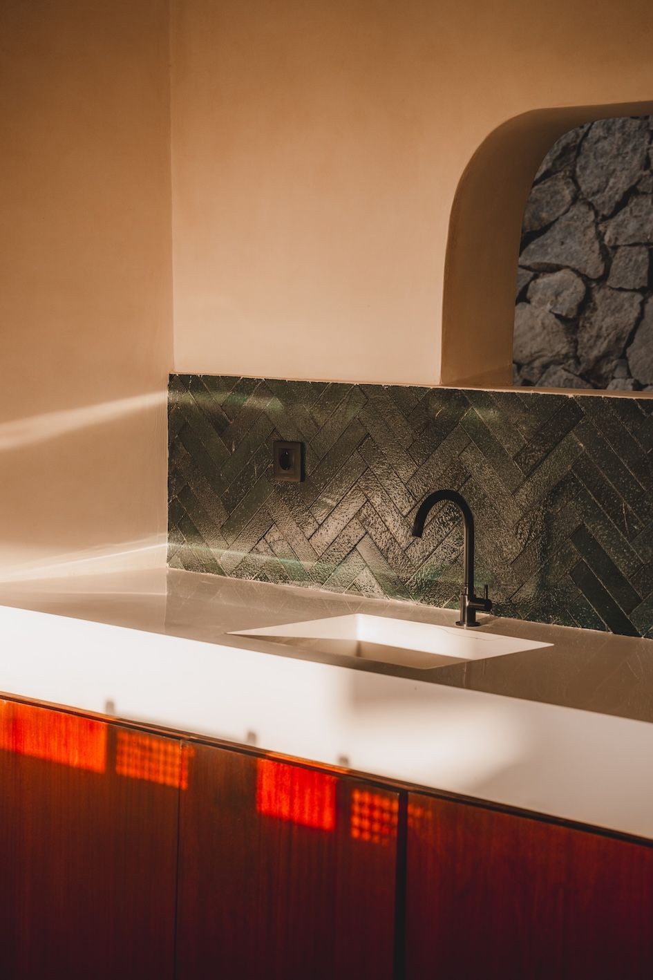 Modern kitchen sink with white countertop, black faucet, and stone backsplash with warm ambient lighting