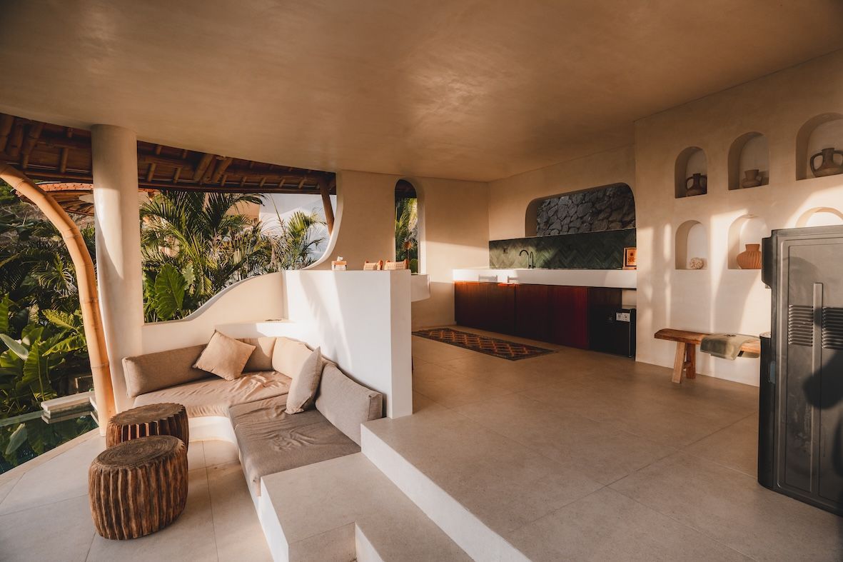 Open-air patio with wicker chairs, beige cushions, white walls, and a built-in bar at sunset