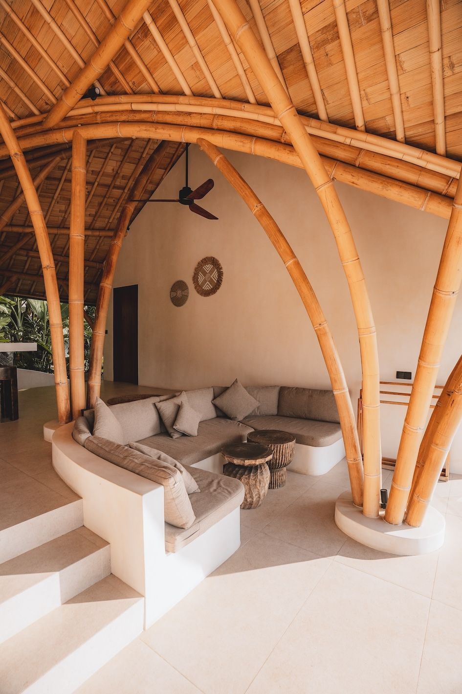 Open-air bamboo lounge with beige sectional sofa, coffee table, and woven thatched roof