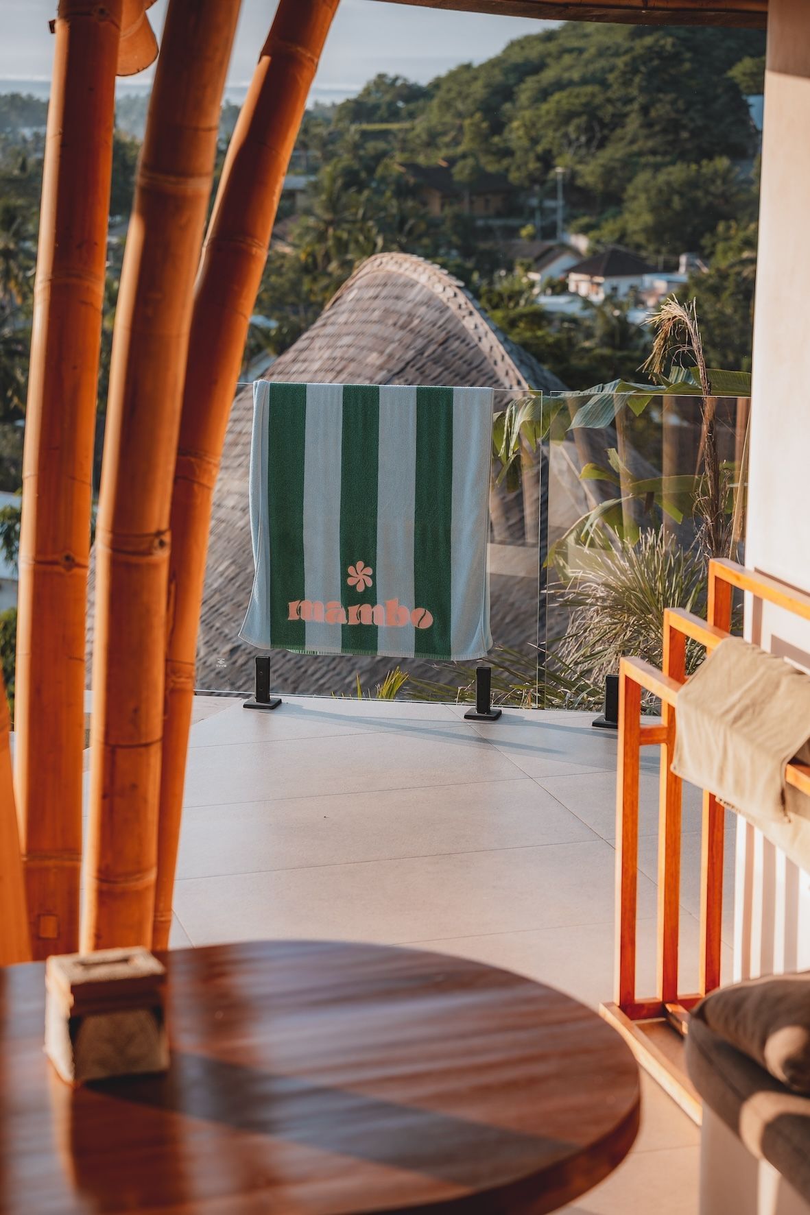 Terrace view with a striped umbrella, bamboo poles, and a round table overlooking green hills and distant houses