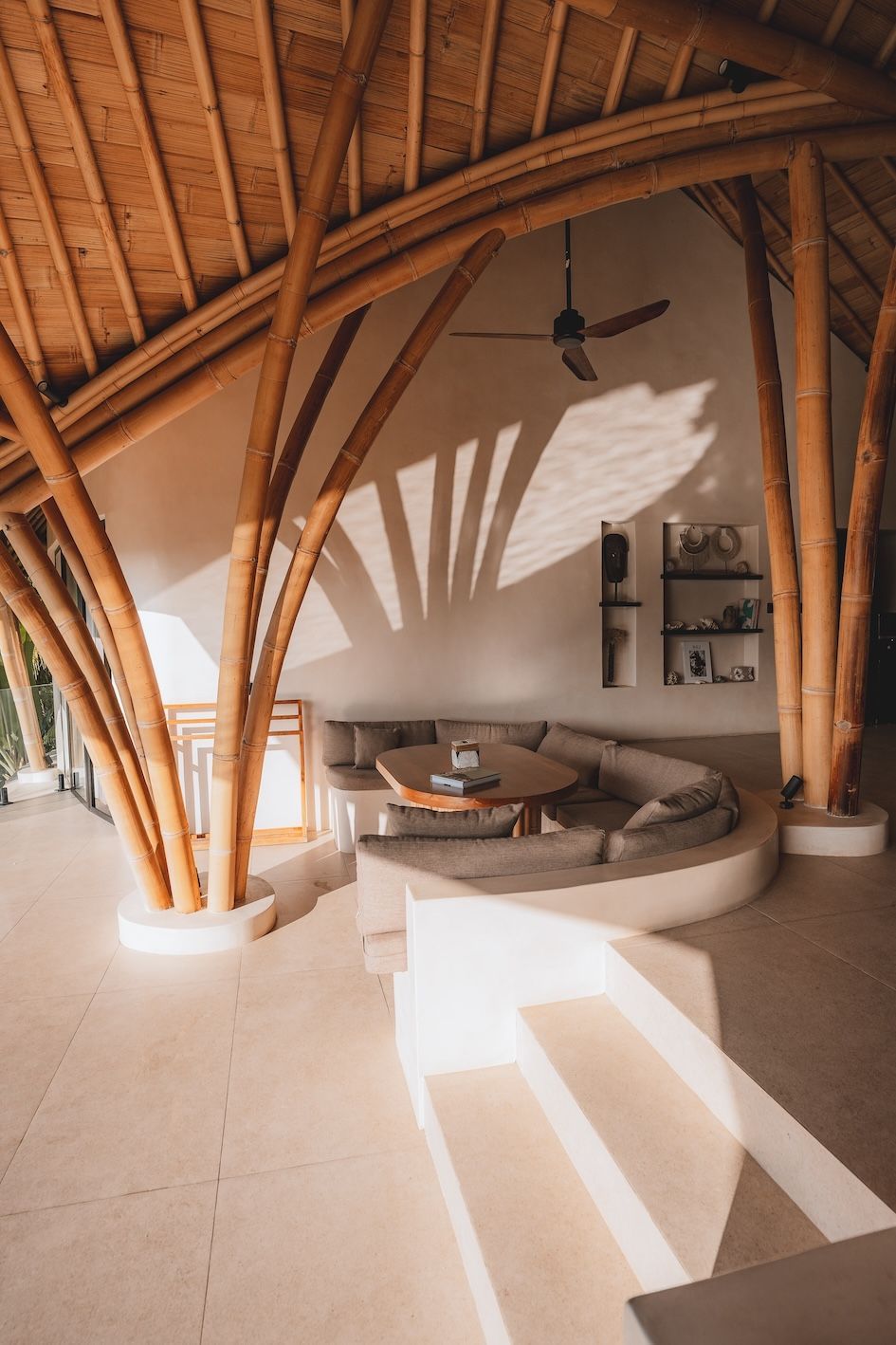 Sunny bamboo-roof lounge with curved sofa, white walls, and patterned sunlight on the floor