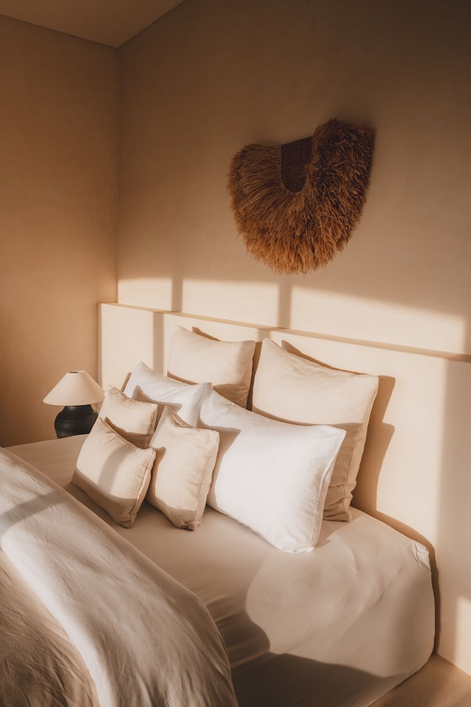 Cozy beige bedroom with a neatly made bed, white pillows, bedside lamp, and heart-shaped wall decor