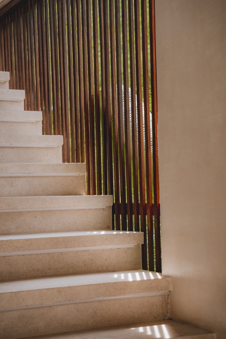 Indoor staircase with beige steps beside a decorative vertical wooden slat wall.