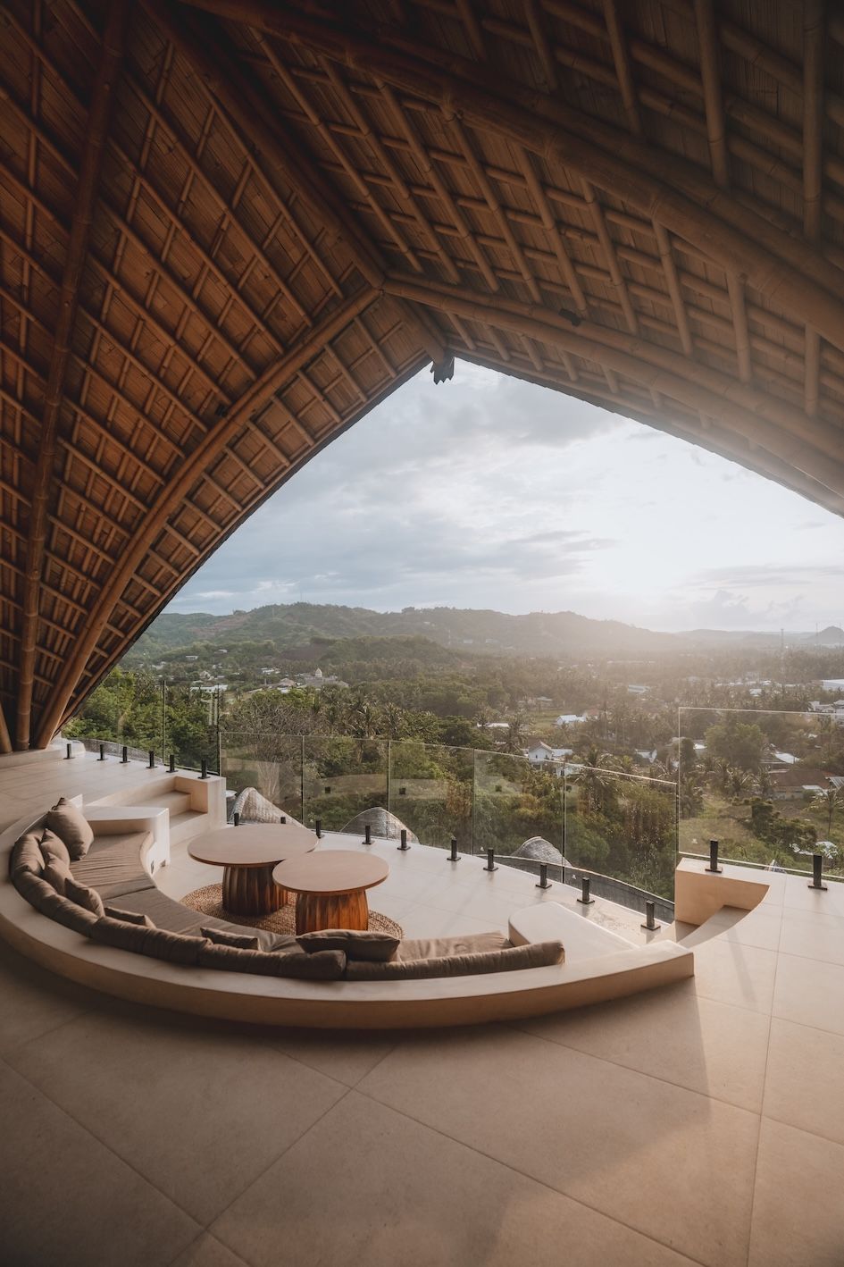 Open-air terrace under a thatched roof overlooking a lush valley at sunset