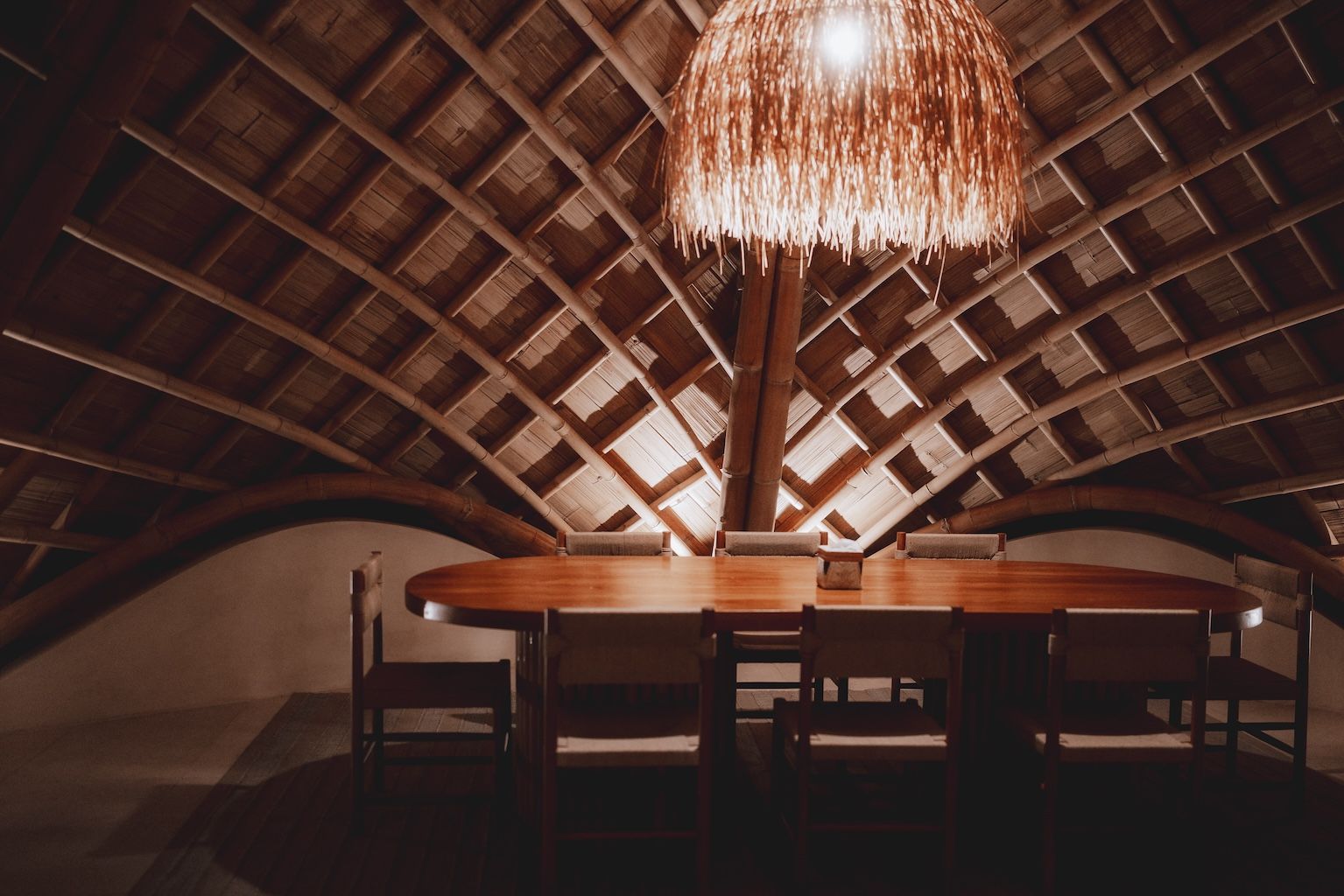 Rustic dining room with a long table, chairs, and a dramatic thatched vaulted ceiling chandelier
