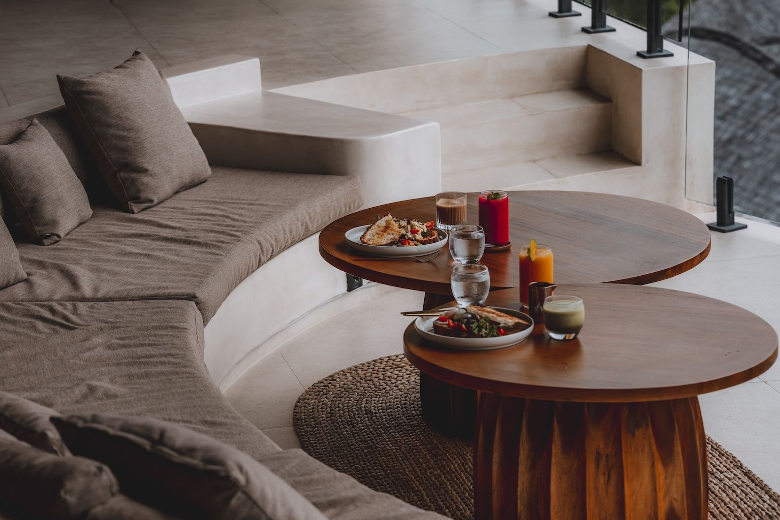 Cozy lounge with curved brown sofa and round wooden coffee tables set with drinks and trays
