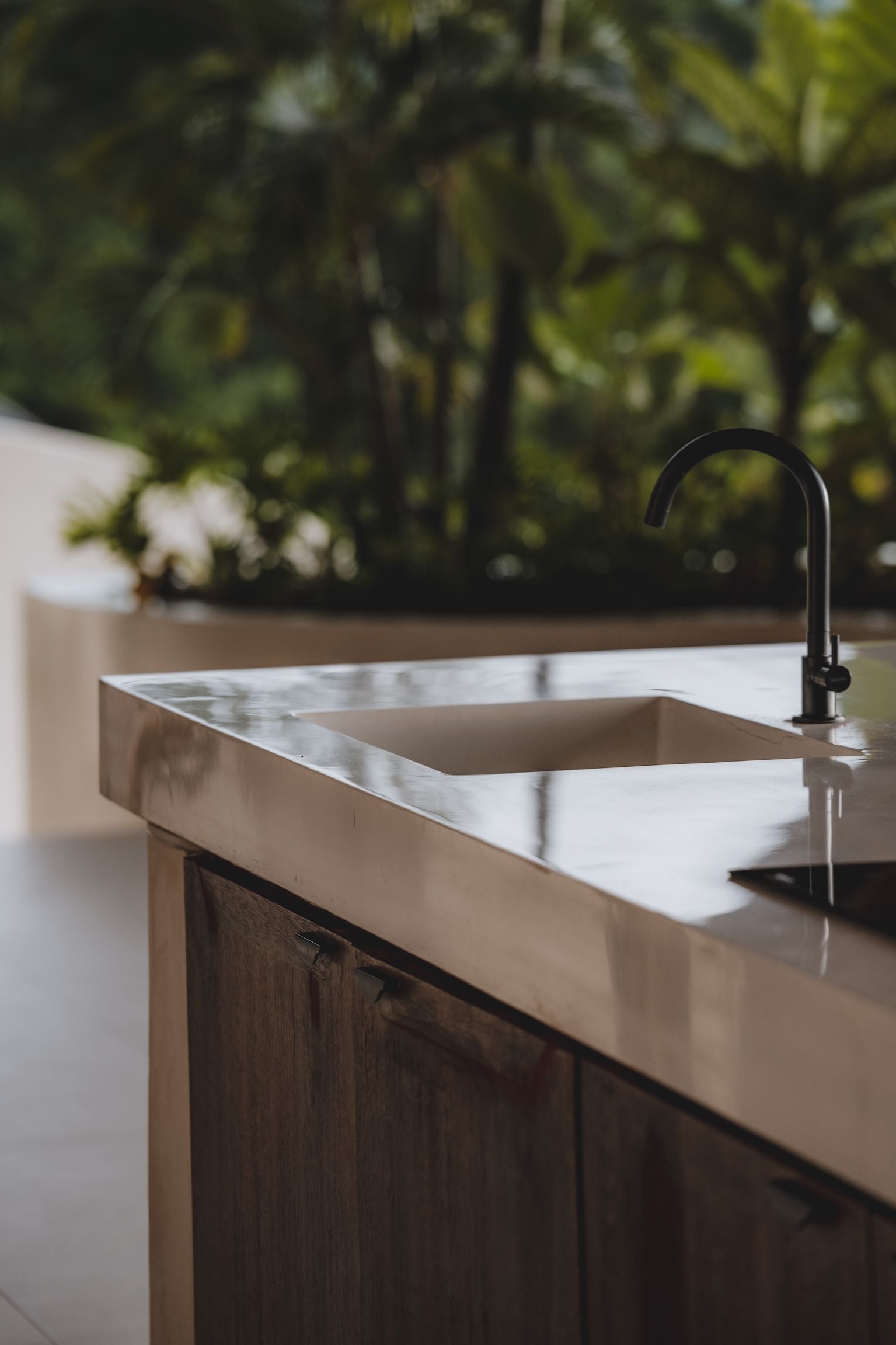 Modern kitchen sink with faucet and light countertop, blurred greenery outside the window