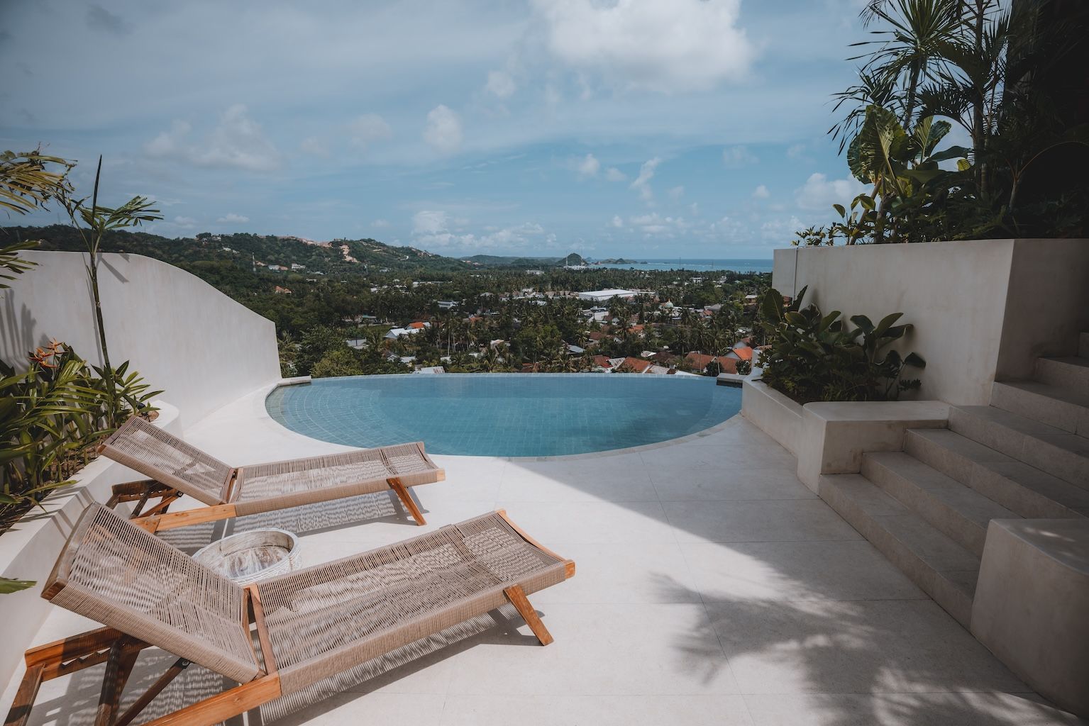 Infinity pool and lounge chairs overlooking a tropical hillside and ocean view