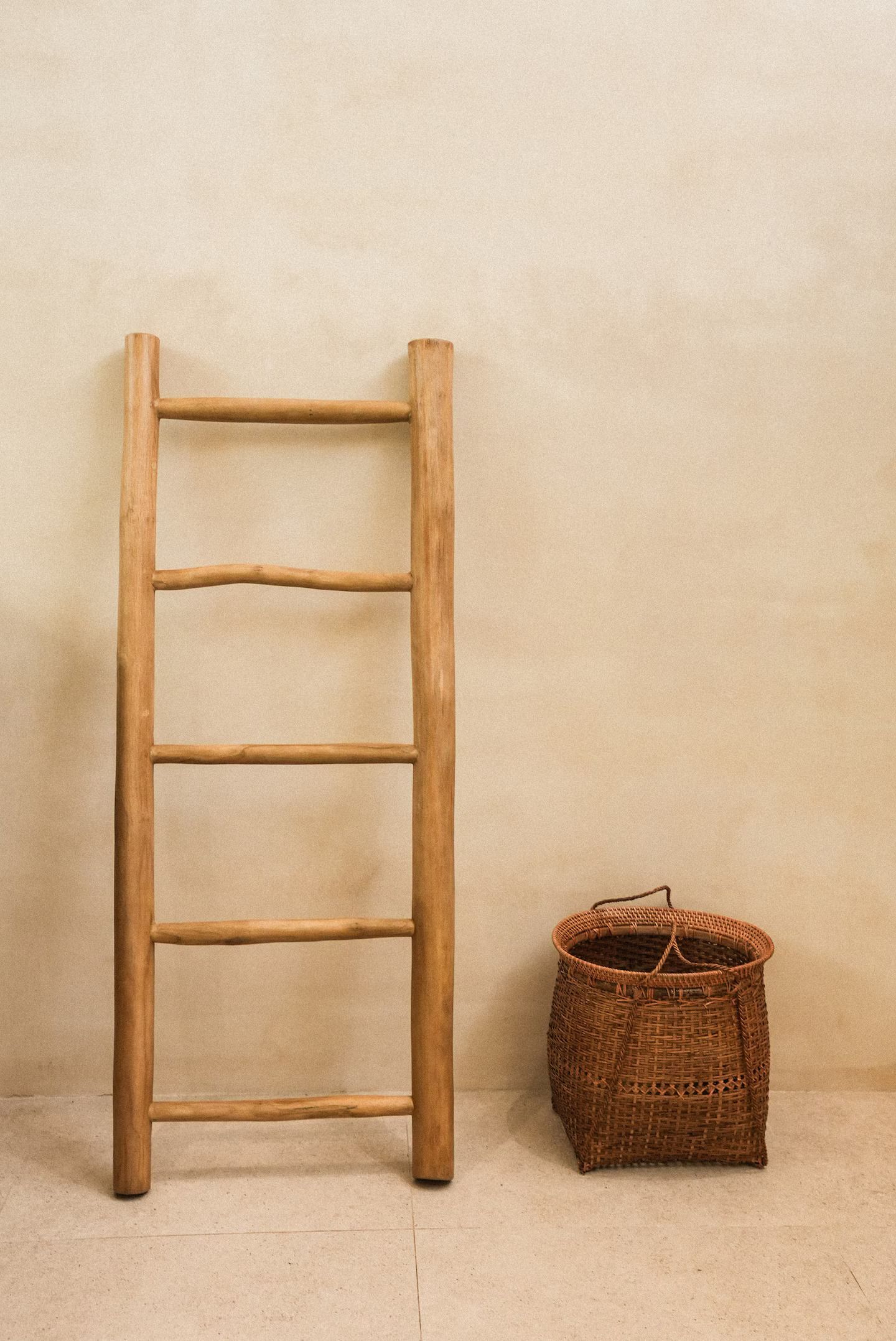 Wooden ladder leaning against a beige wall beside a woven basket on a bare floor