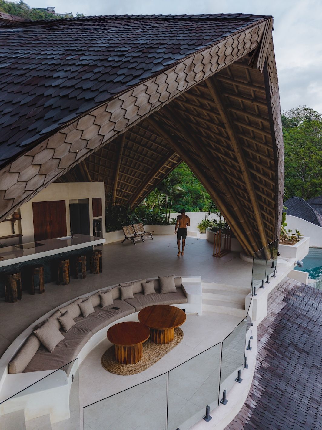 Open-air resort lounge with curved sofas under a large thatched roof, overlooking the water.