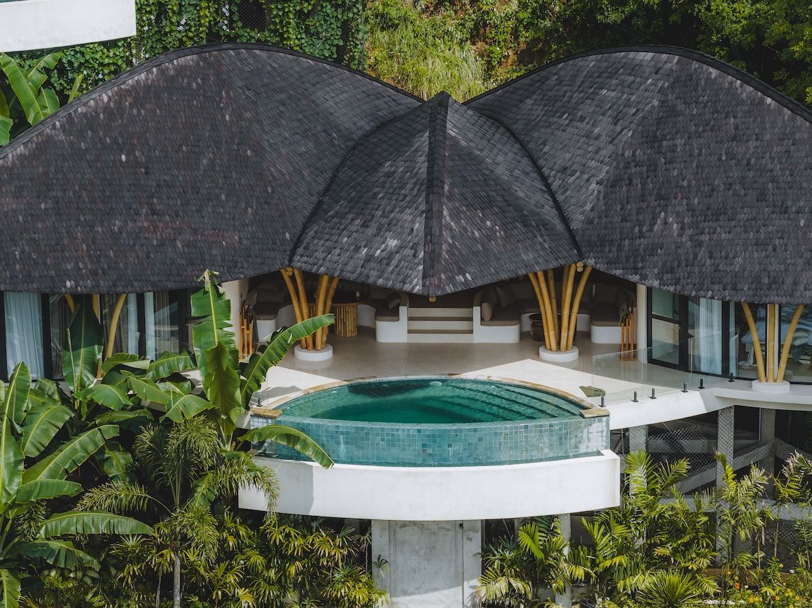 Modern tropical villa with dark thatched roofs and a central round pool surrounded by lush greenery