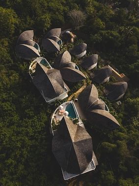 Aerial view of a cluster of modern thatched-roof villas surrounded by dense green forest