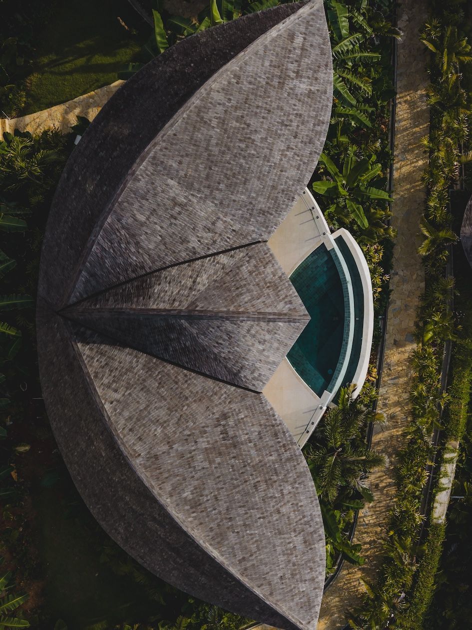 Aerial view of a circular thatched-roof building with a central pool, surrounded by tropical greenery.