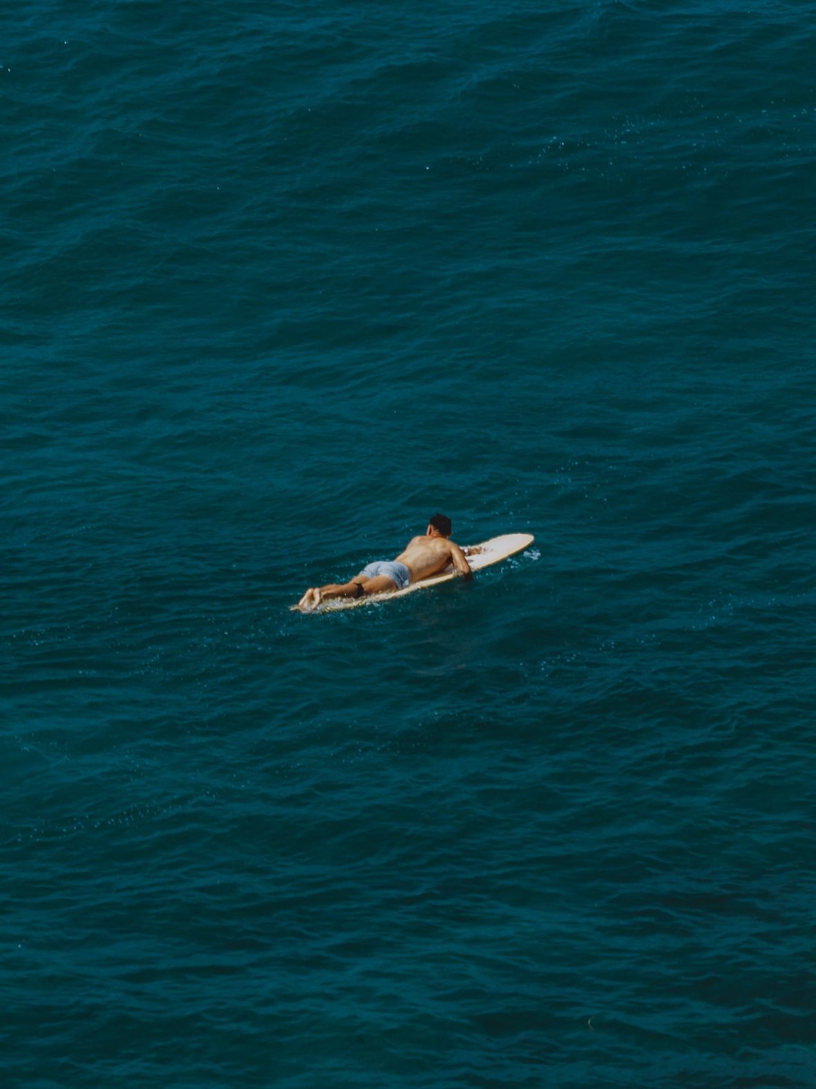 Person lying on a white surfboard in deep blue ocean water