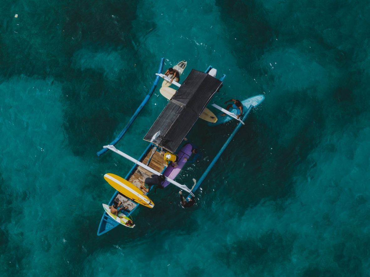 Aerial view of a small boat with colorful outriggers on clear turquoise water