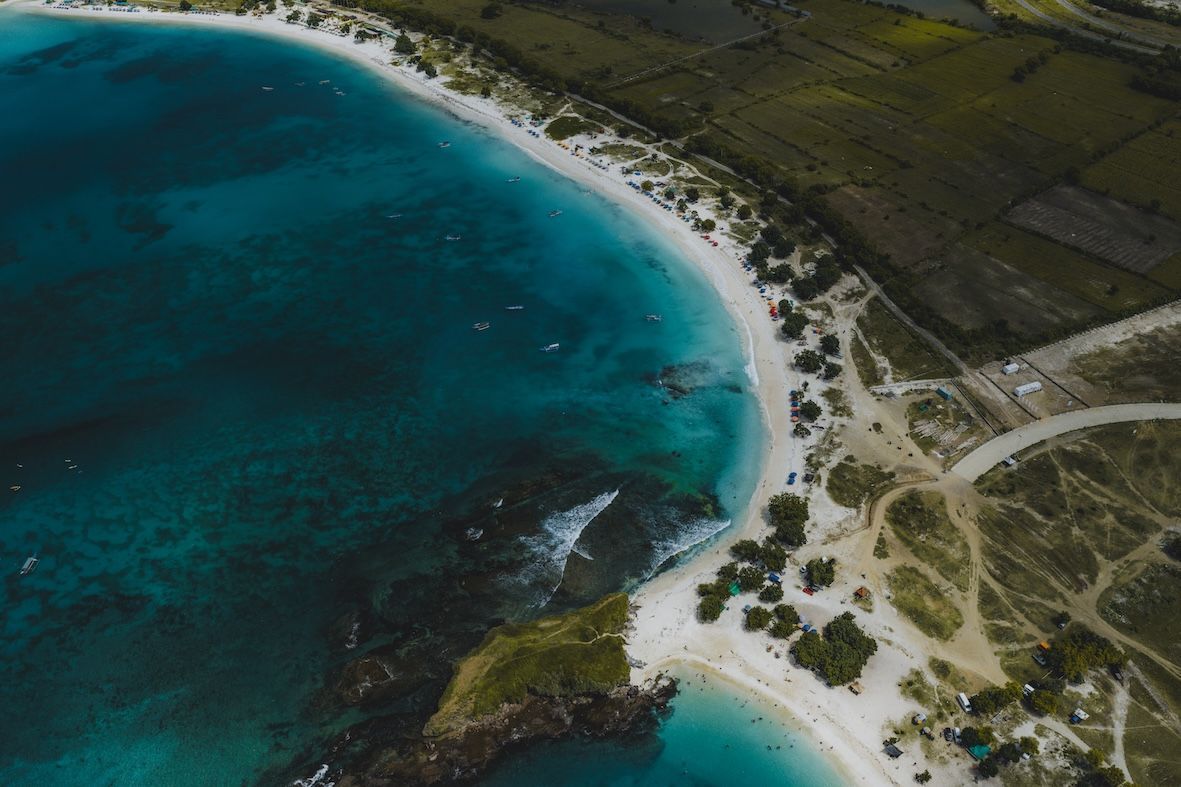 Aerial view of a turquoise bay with sandy shore and green coastal land.