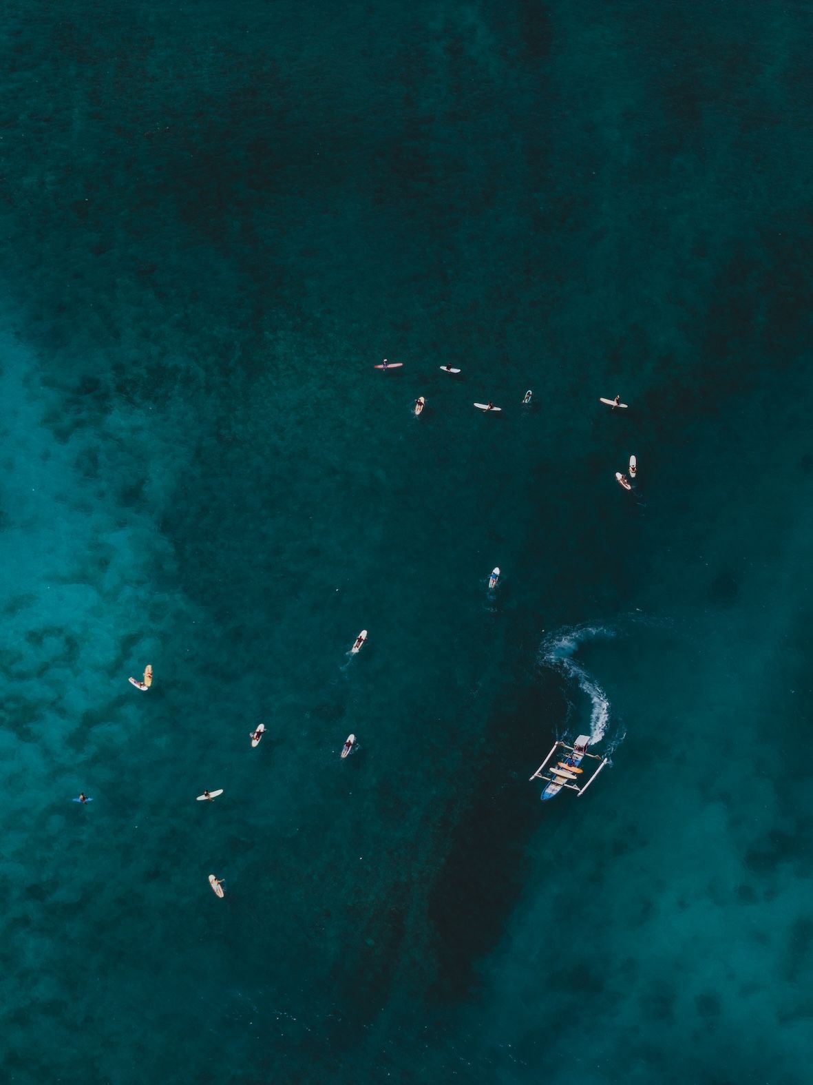 Aerial view of swimmers and a small boat in dark blue-green water