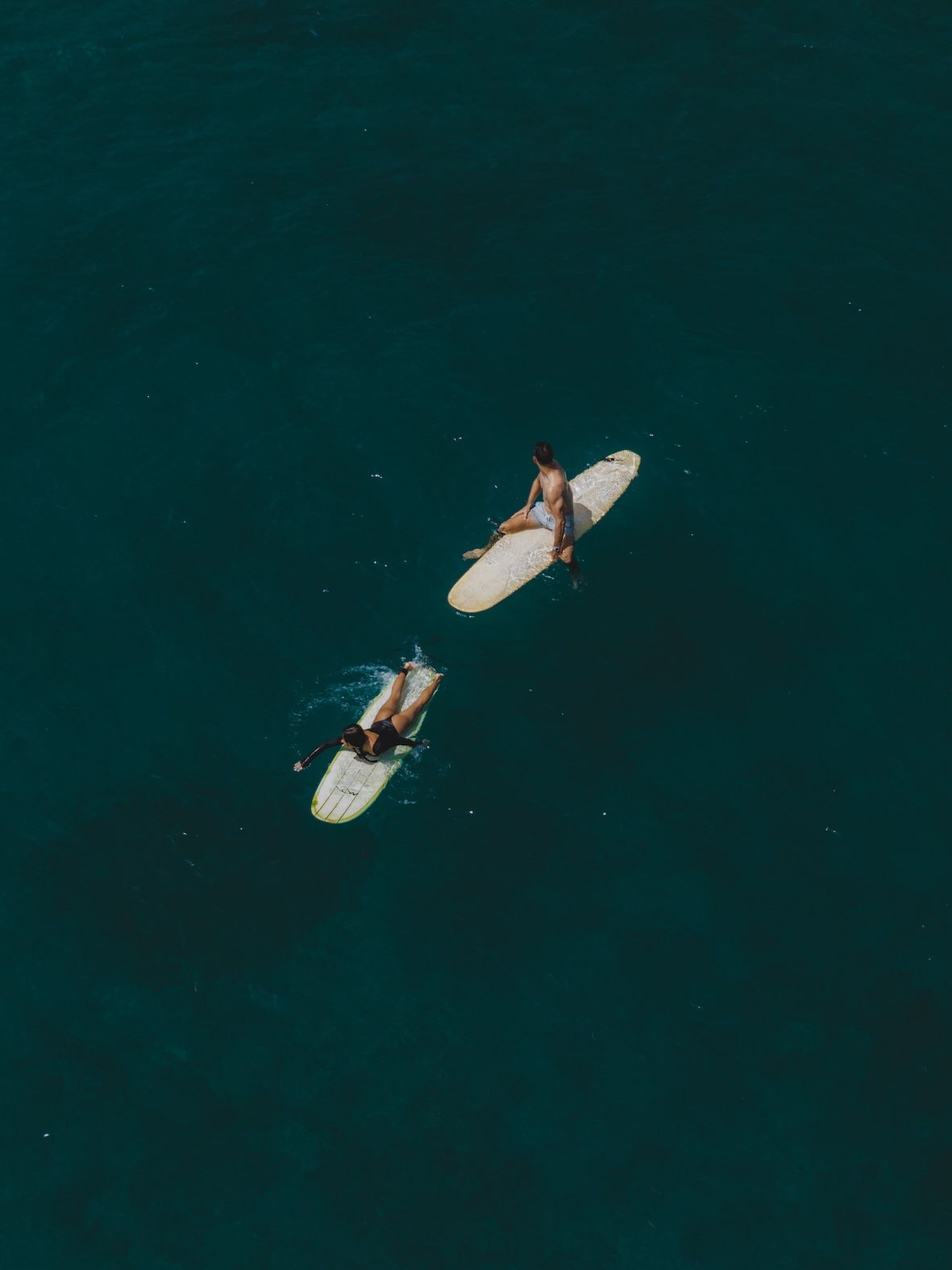 Two people on surfboards floating in dark green water