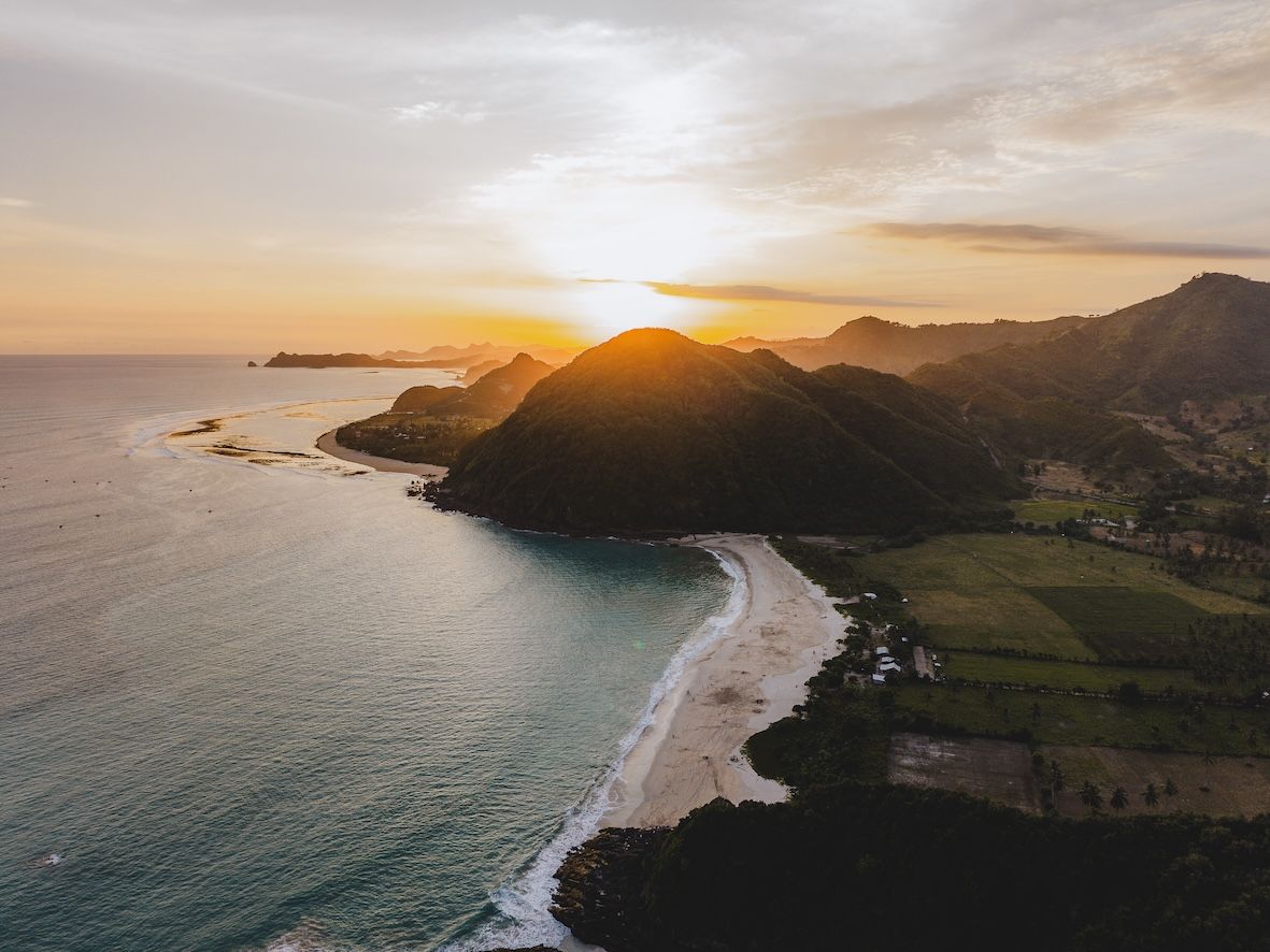 Sunset over a coastal beach with cliffs, waves, and green farmland below