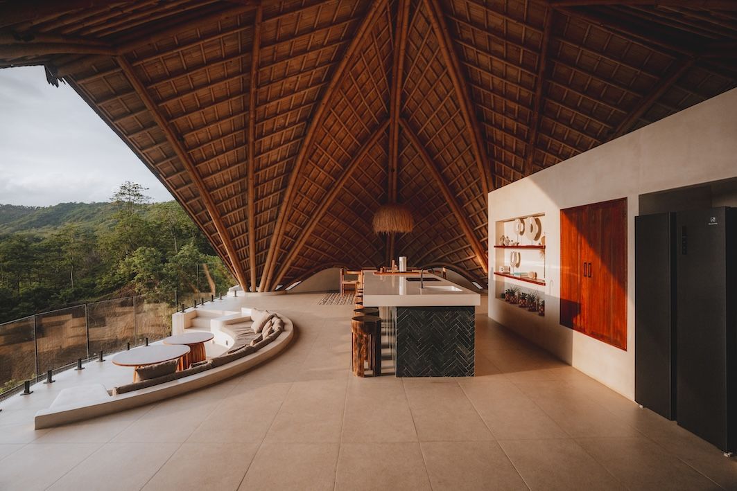 Open-air lounge with a thatched roof, curved seating, and forest view