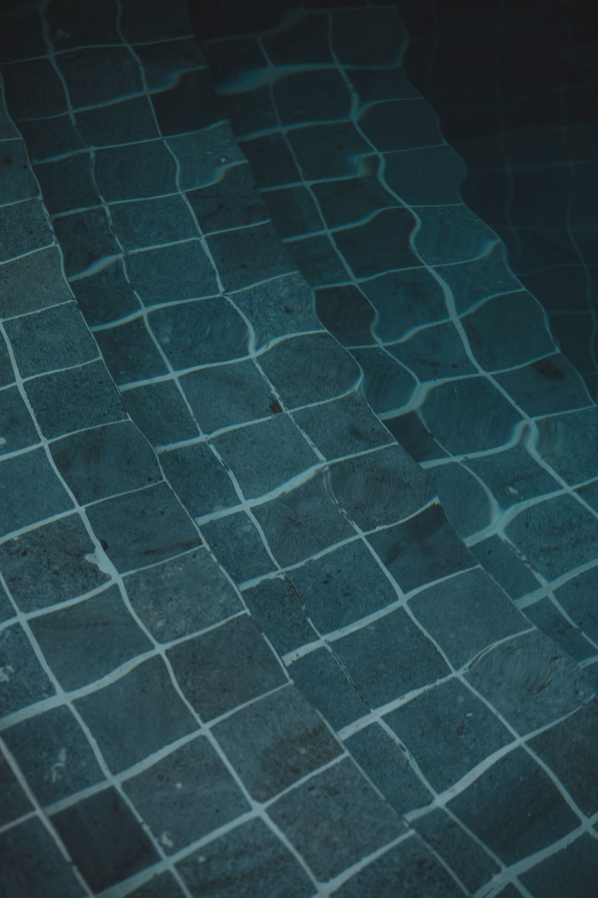 Dark teal tiled floor with a grid of pale grout lines and wavy reflections from light above