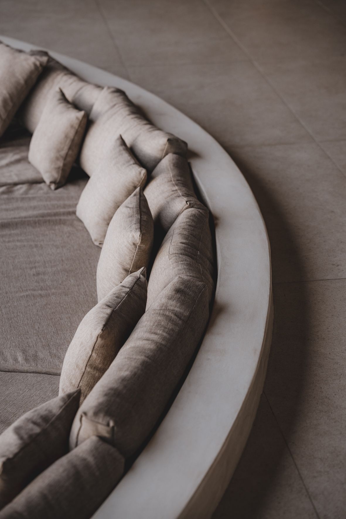 Curved beige sectional sofa with matching throw pillows on a tiled floor