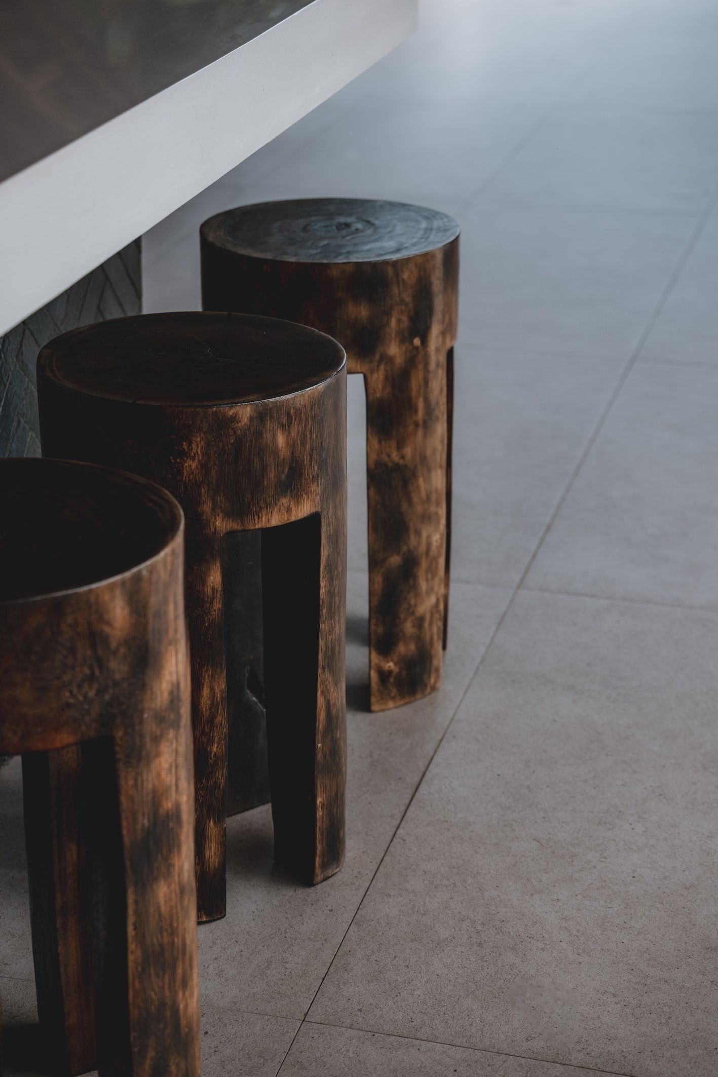 Three rustic wooden stools beside a wall on a light gray tiled floor