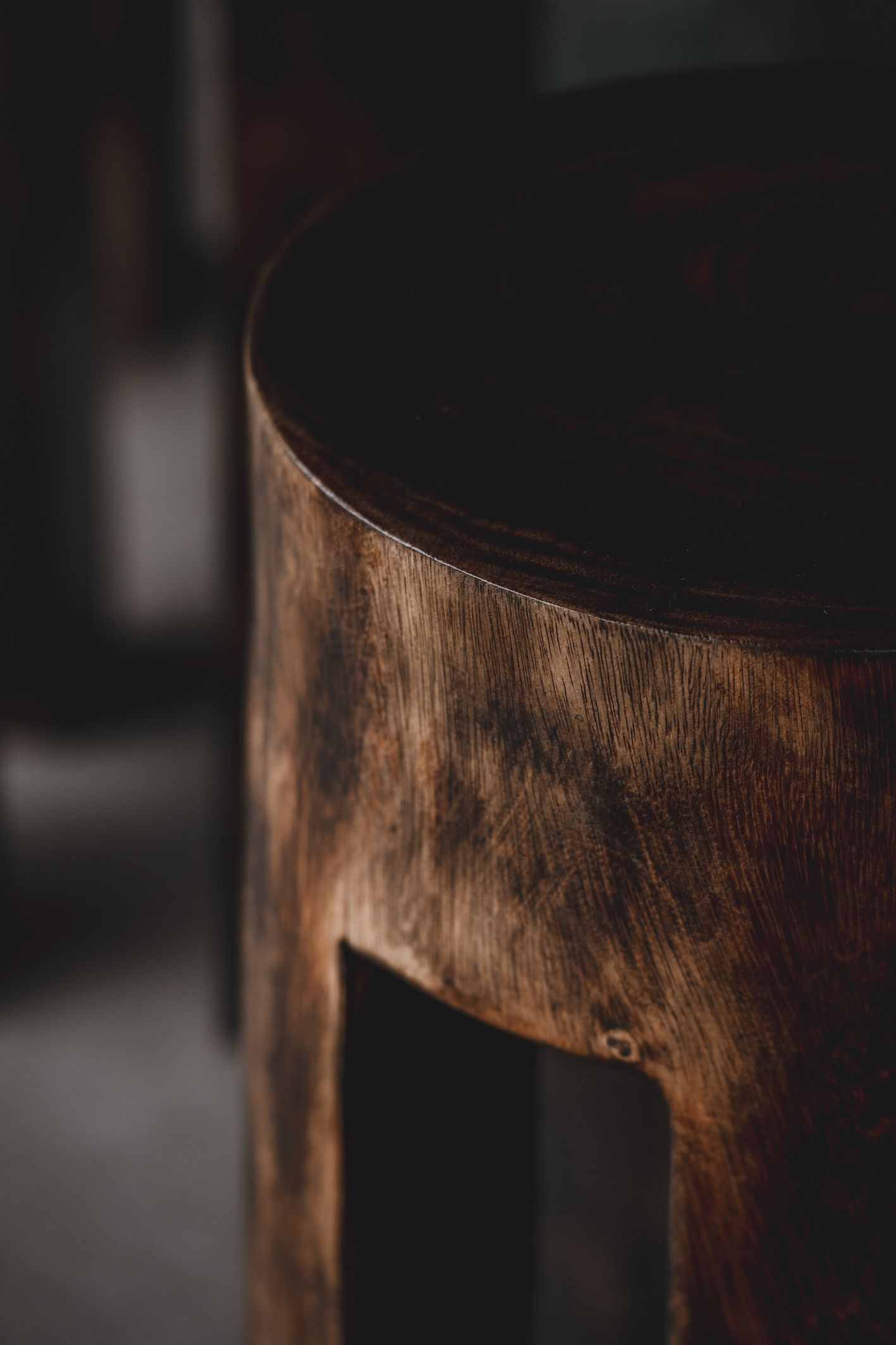 Close-up of a rustic wooden stool with a dark round seat and weathered brown legs.