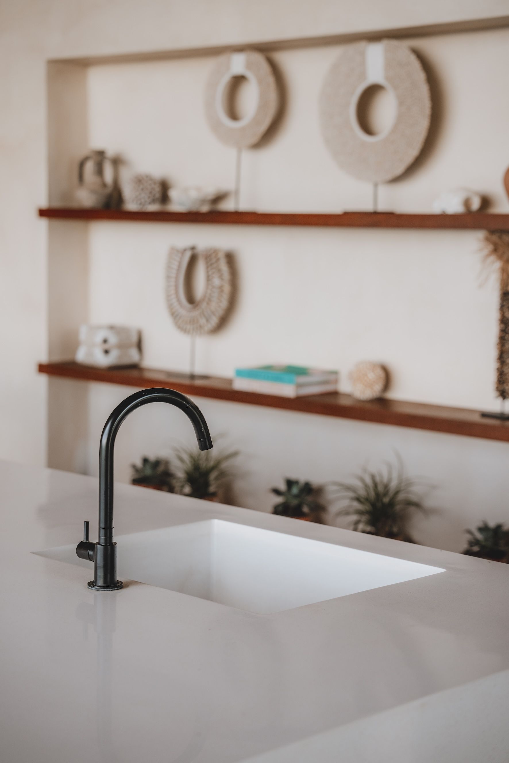 Modern kitchen with white counters, black faucet, and wooden shelves holding decor and plants.