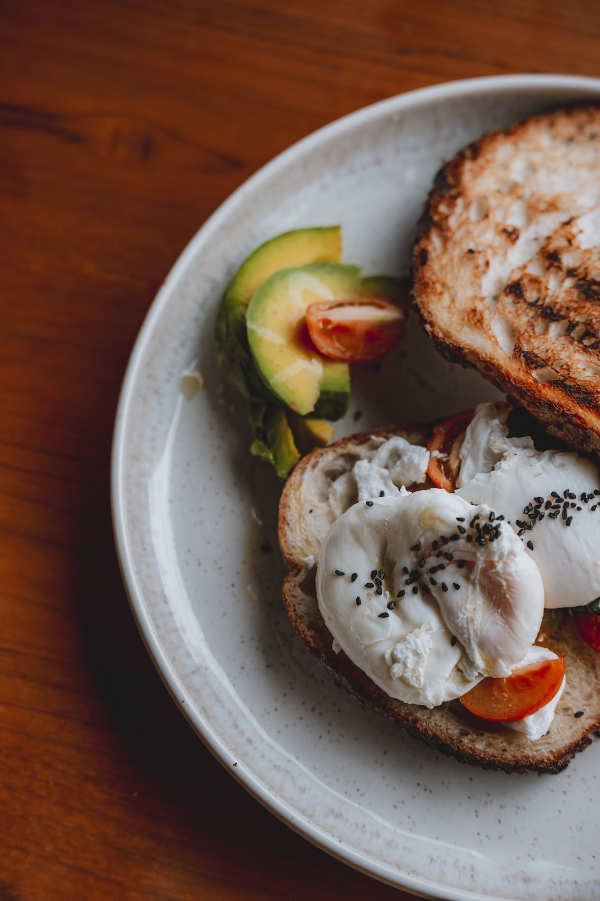 Plate with avocado toast, poached egg, and sliced fruit on a wooden table