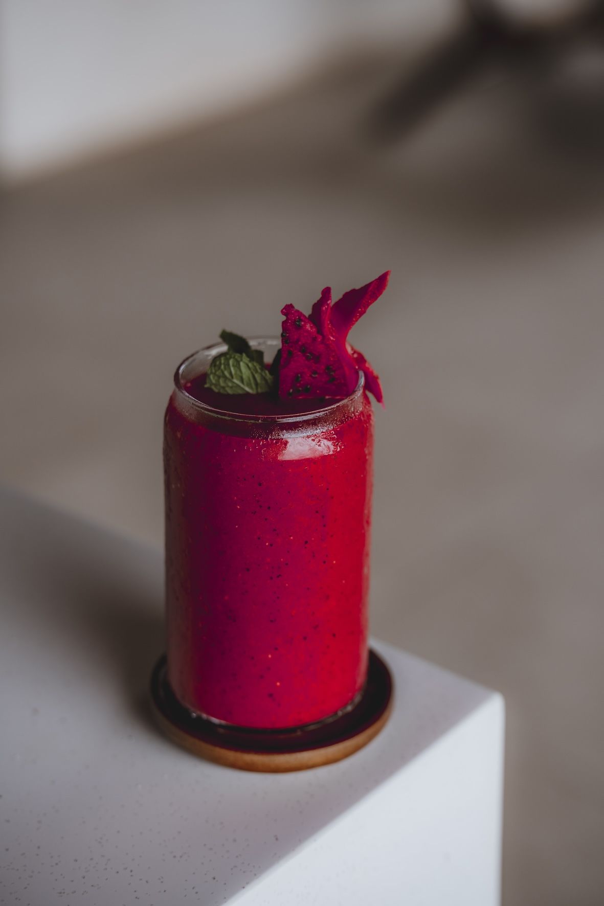 Magenta cocktail in a tall glass with mint garnish on a white pedestal