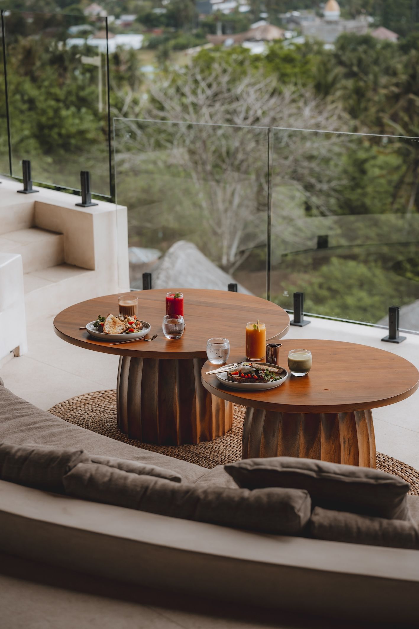 Balcony seating with two round wooden tables set with drinks, overlooking a lush green valley