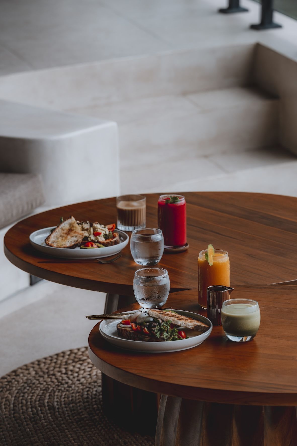 Two plates and drinks on a round wooden table in a modern lounge area