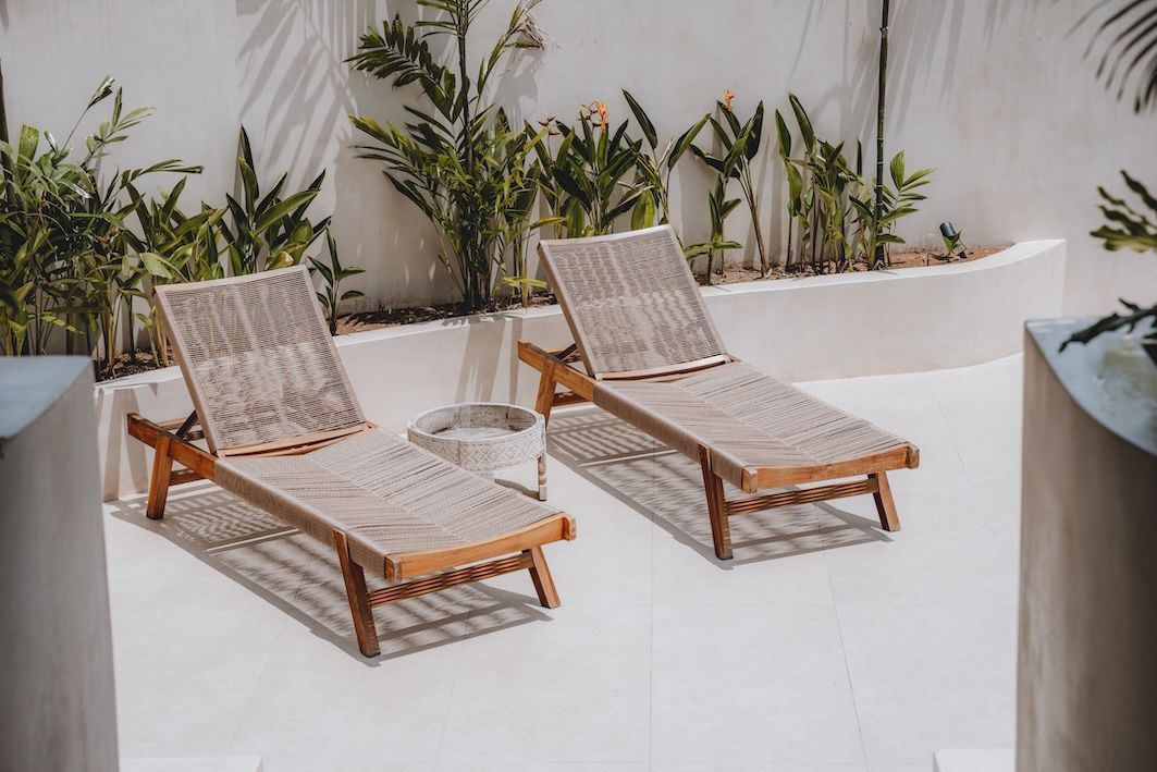 Two woven lounge chairs on a bright patio with white walls and potted plants.