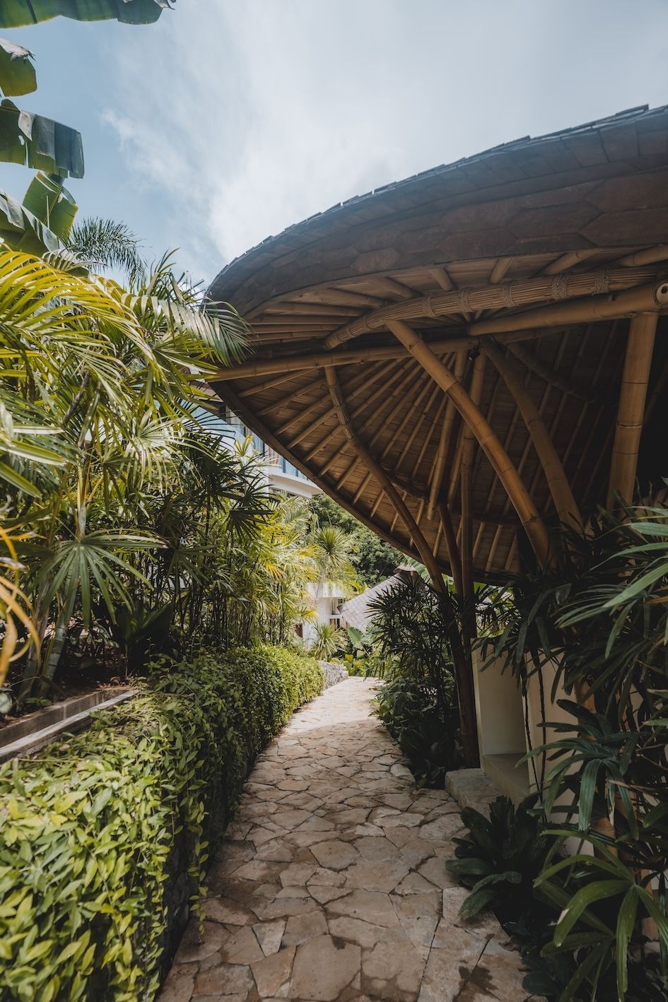 Tropical stone path beside lush greenery and a thatched-roof hut under a bright sky
