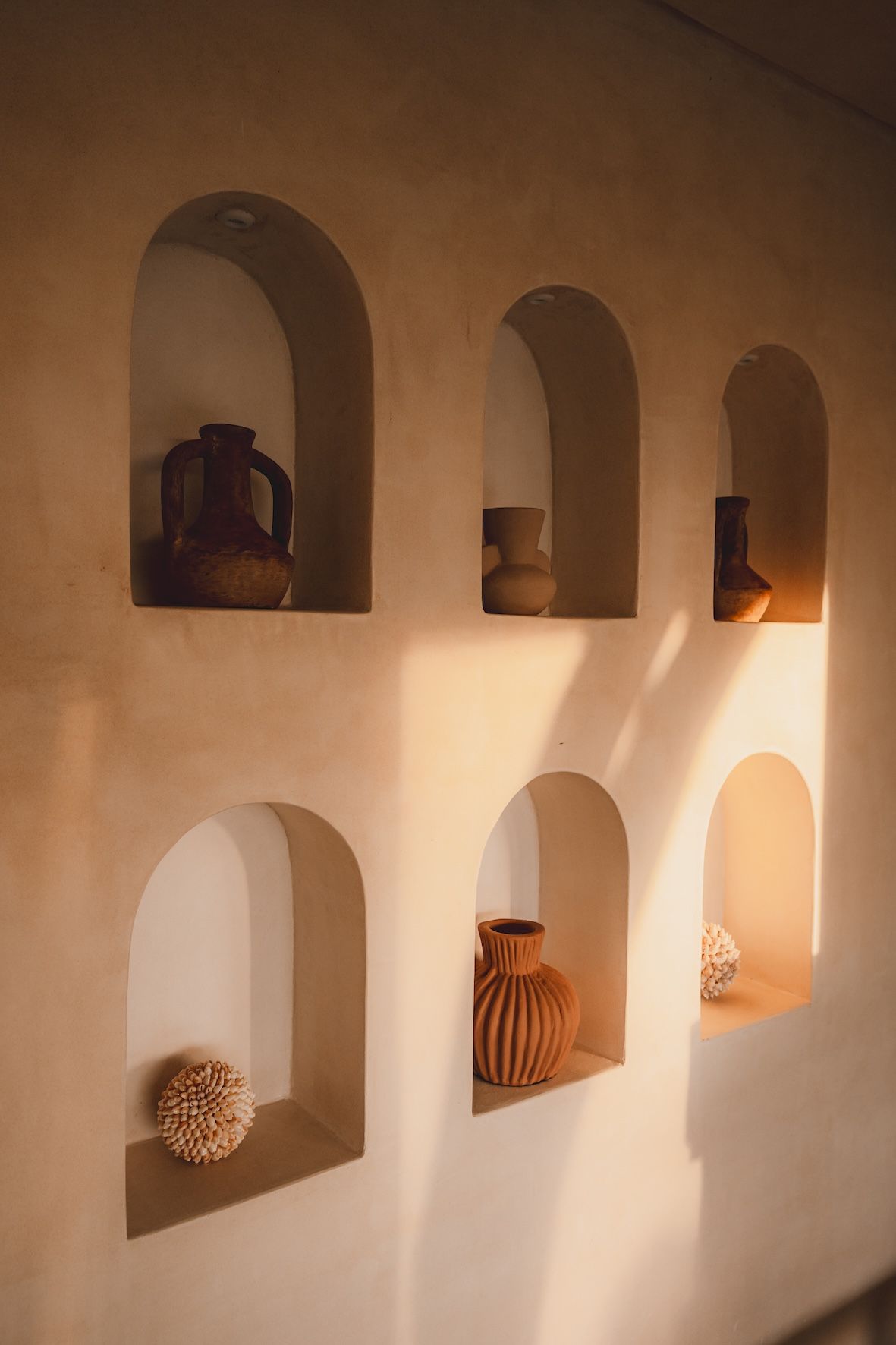 Warm-toned wall niches with woven baskets and pottery, lit by soft sunlight and shadows