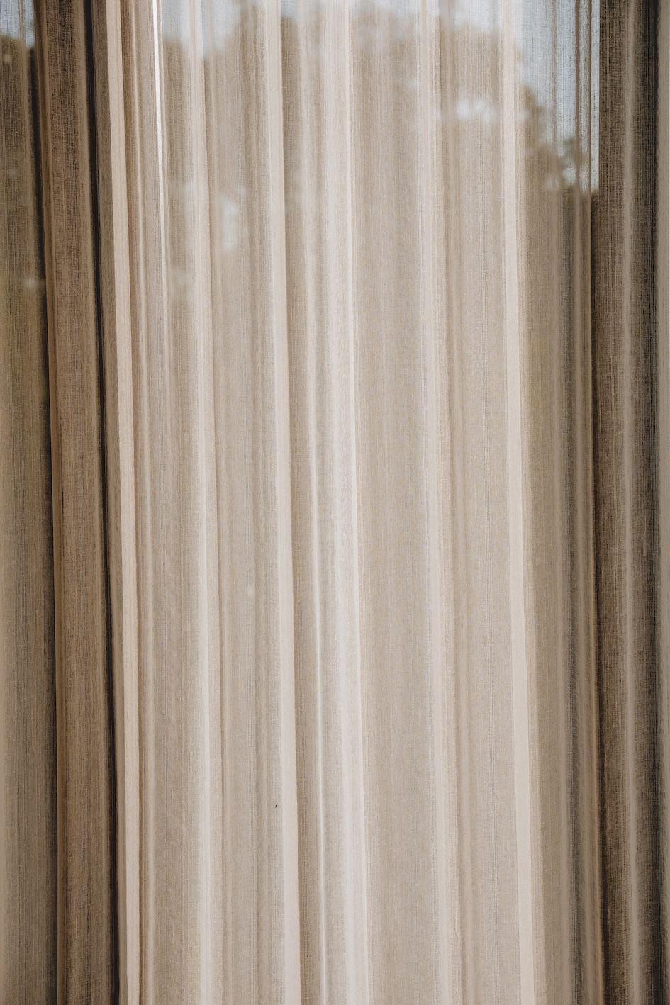 Vertical beige and brown striped curtain or drape hanging by a window