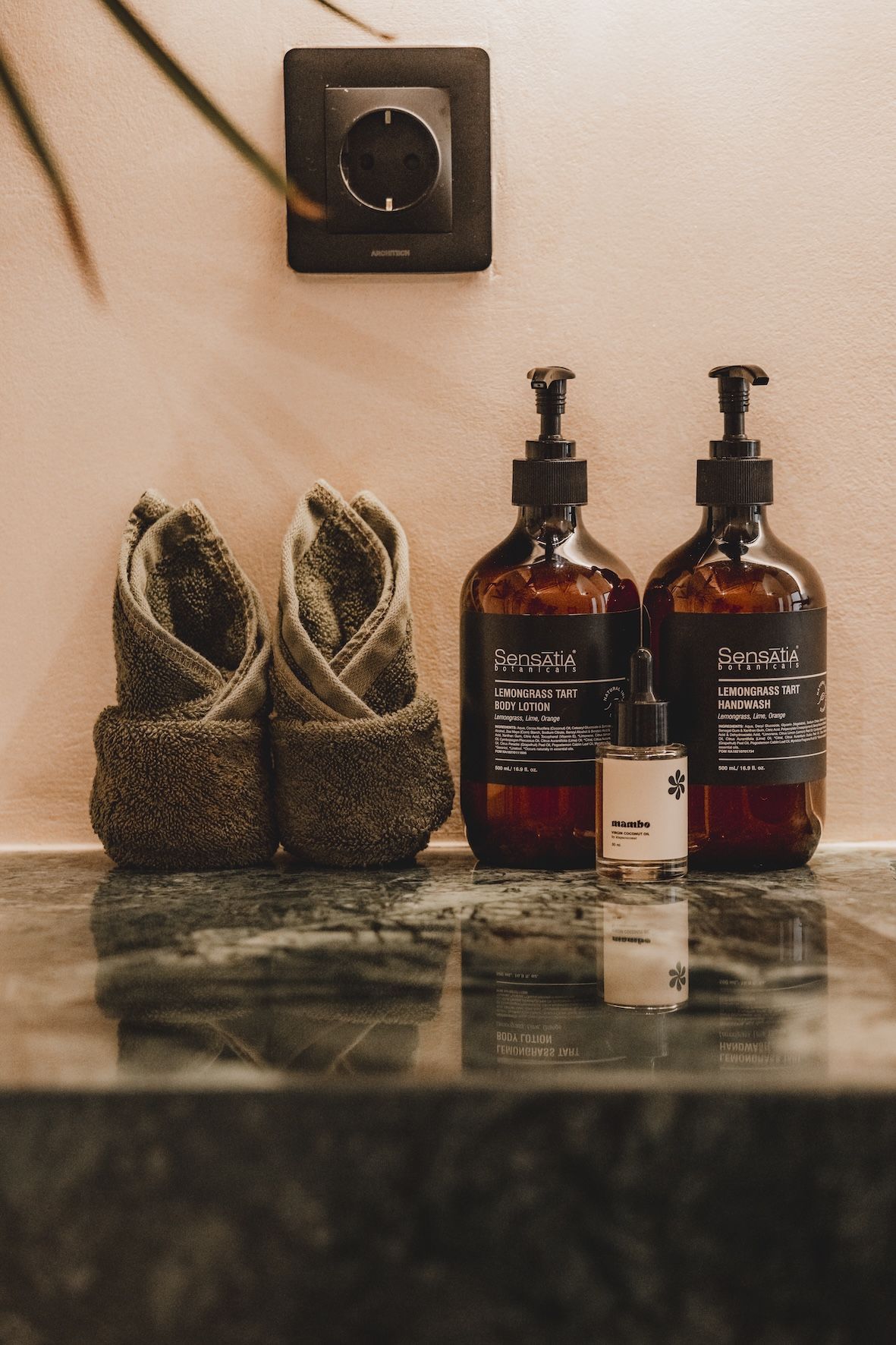 Spa toiletries and rolled towels on a marble countertop beneath a wall switch.