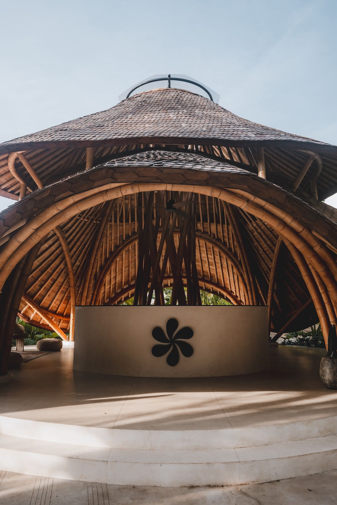Open-air wooden pavilion with a woven roof and flower emblem on the front wall