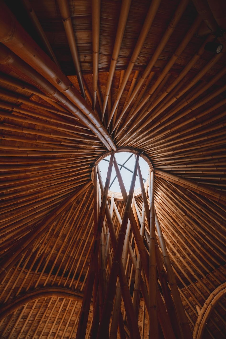 Upward view of a woven wooden dome with sunlight streaming through the center opening