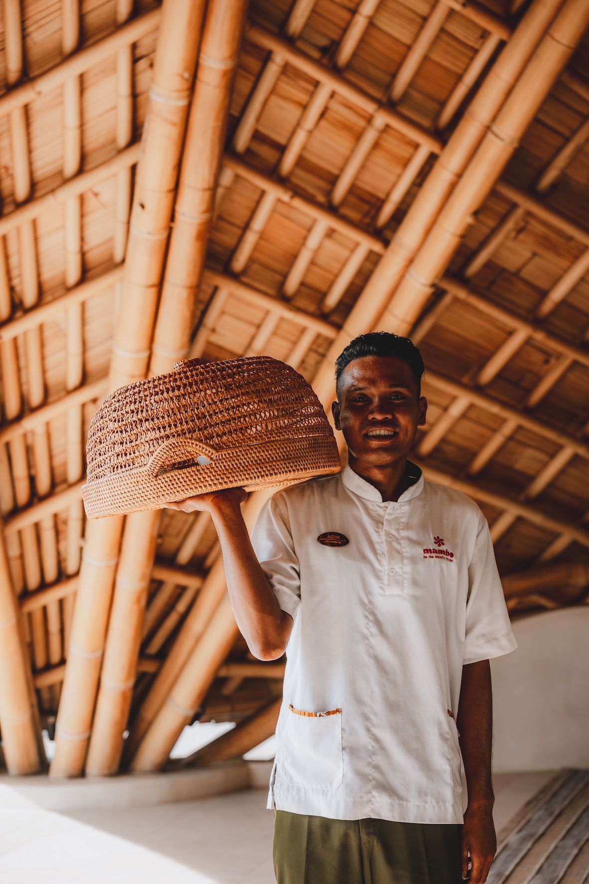 Person holding a woven basket inside a bamboo-roofed building.