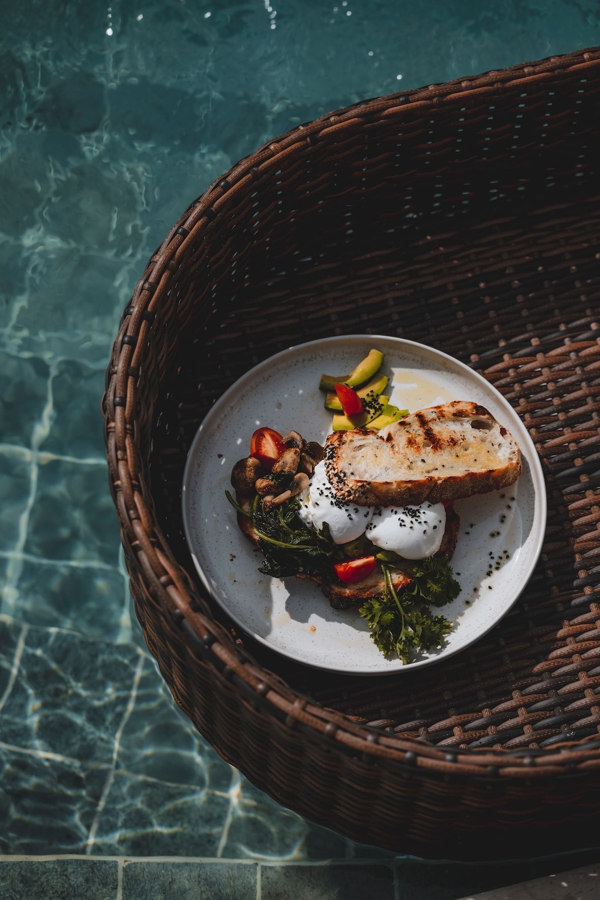 Plated gourmet meal on a woven tray beside turquoise pool water