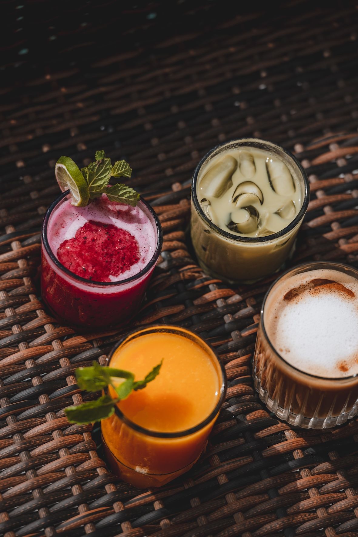 Four colorful cocktails in glasses on a dark woven table