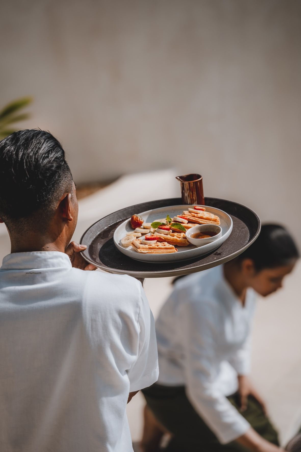 Waiter carrying a tray with plated food while another person walks down a stairway